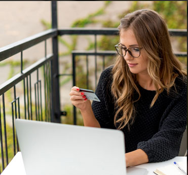 A woman in a black shirt and glasses reads information from her credit card to put into her laptop for payment processing.